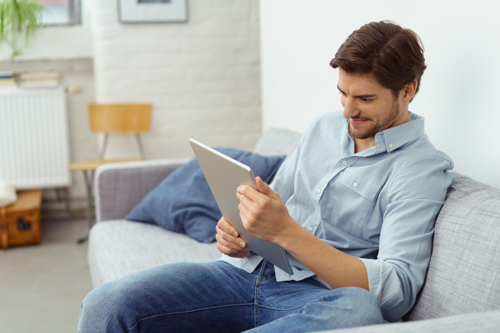 mann sitzt auf dem sofa und schaut auf sein tablet