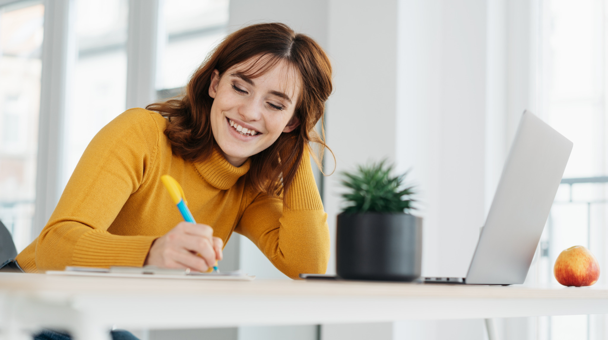 Happy young woman sitting writing or designing at an office table with a cheerful happy smile in a low angle view with copy space