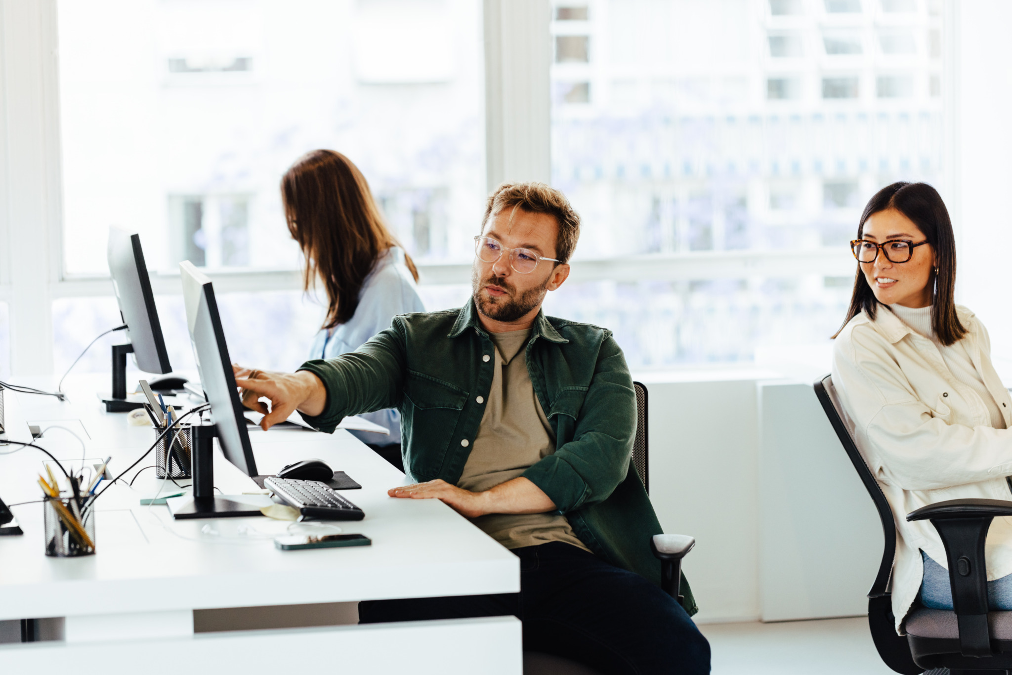 Male software designer talking to his colleague while working at his desk in an office. Business man pointing at his computer screen and discussing his project.