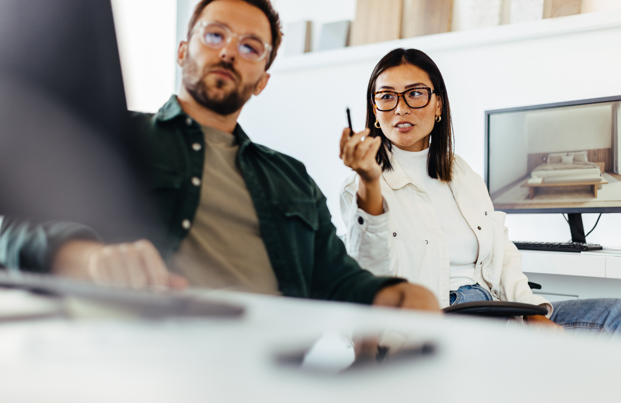 Interior designers looking at a computer screen while discussing a project. Two business people talking to each other while sitting at their desks in an office.