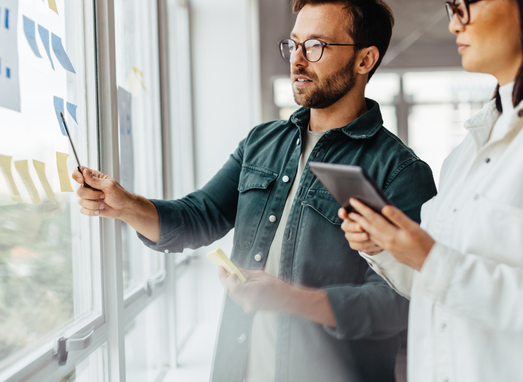 Creative business people brainstorming with sticky notes in an office. Business professionals standing next to a window and discussing their ideas.