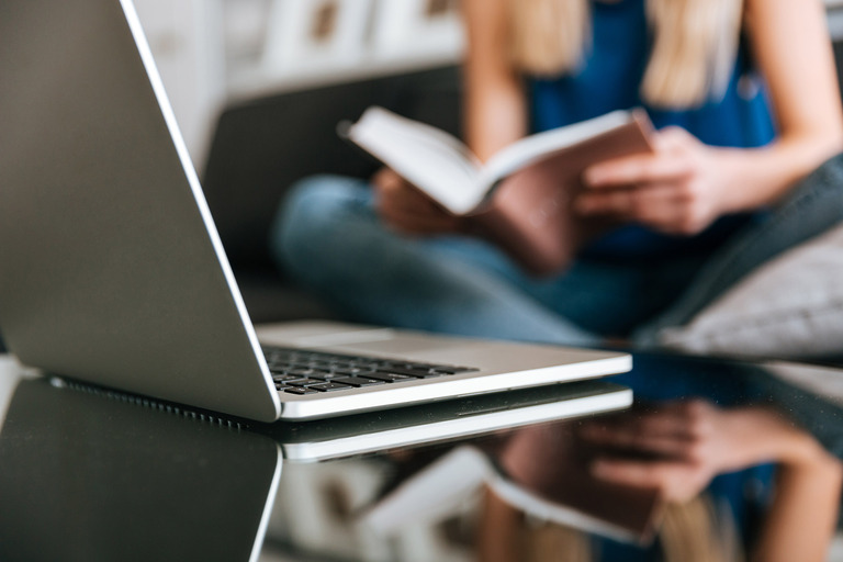 laptop-table-near-woman-reading-book-home