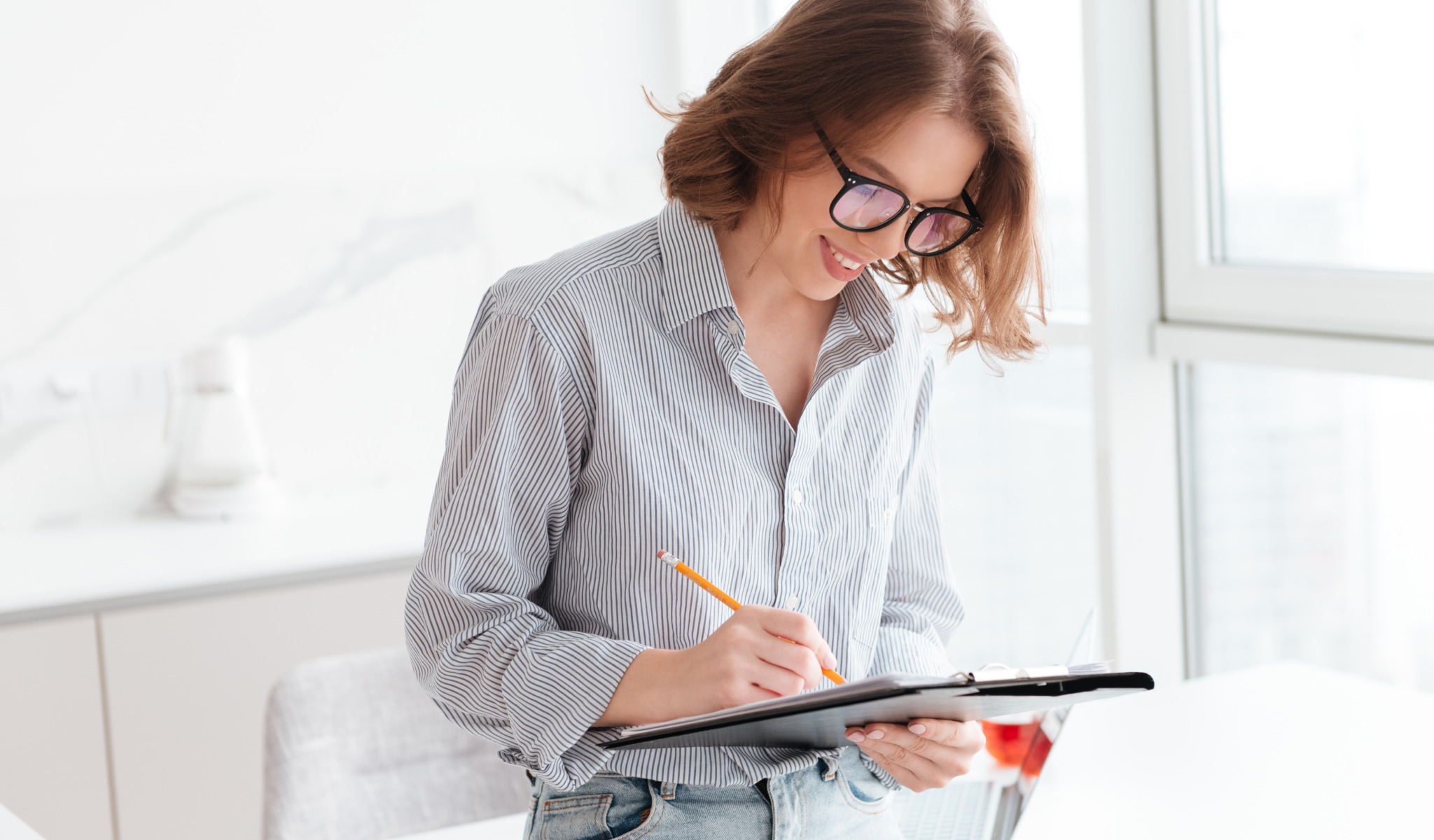 Smiling young woman writing on a clipboard while standing at home